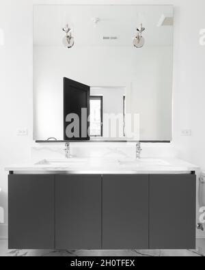 A luxurious bathroom with a grey vanity cabinet, white marble countertop, lights mounted on the mirror, and a black door. Stock Photo