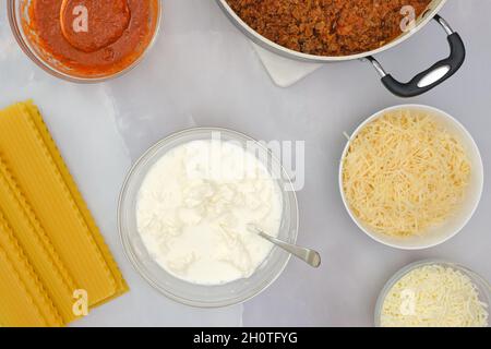 Raw lasagna noodles, ground beef on frying pan, marinara, and cheese in bowls. Step by step beef lasagna recipe, ingredients close up on kitchen table Stock Photo
