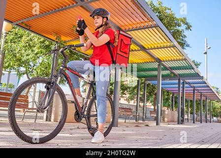 A cyclist delivery woman checks the order address on her smartphone Stock Photo