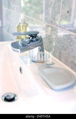 close up of bathroom sink, tap, soap dish and hand soap with grey tiles Stock Photo