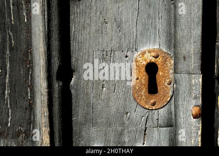 A close up of an old rusty metal keyhole on an old wooden door Stock Photo