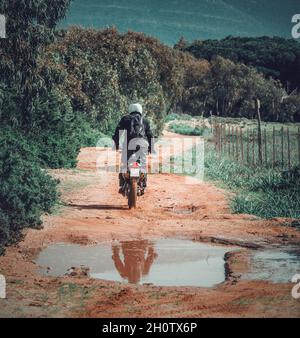 Back view of a biker riding on a dirt road on a sunny day in springtime Stock Photo