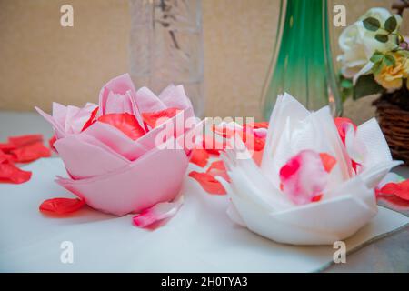 White and pink flowers on napkins. Beautiful origami flower made of napkin on white background . Petals of a red rose. Stock Photo