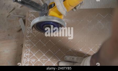 A worker is cutting tiles. Worker cutting a tile using an angle grinder at construction site. Stock Photo