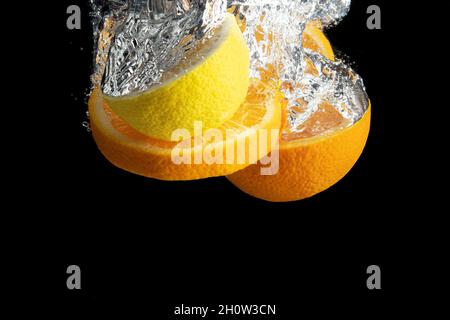 Fresh sliced orange and lemon in water splash isolated on black background. Minimal food concept. Stock Photo