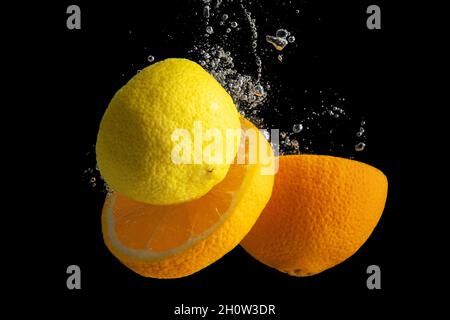 Fresh sliced orange and lemon in water splash isolated on black background. Minimal food concept. Stock Photo