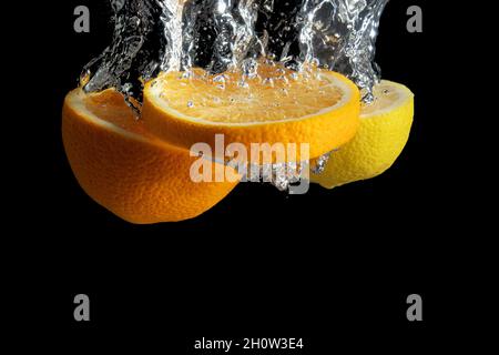 Fresh sliced orange and lemon in water splash isolated on black background. Minimal food concept. Stock Photo