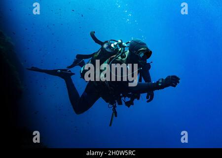 Scuba diver swimming in deep blue blue background Stock Photo