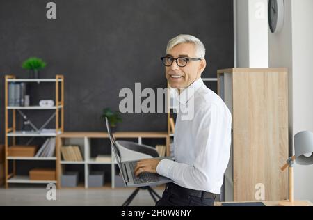 Portrait of senior businessman with laptop in hands working in modern loft office. Stock Photo