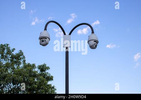 Surveillance cctv (closed circuit television) camera installed in public park on blue sky background for protection against crime, observation of peop Stock Photo
