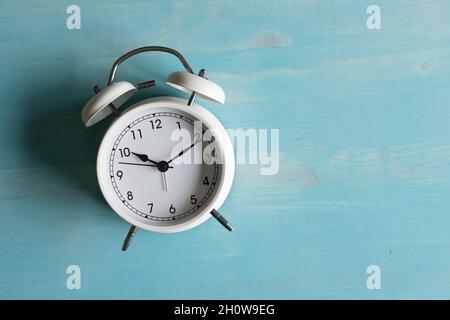 small white retro alarm clock on a blue wood background with copy space Stock Photo