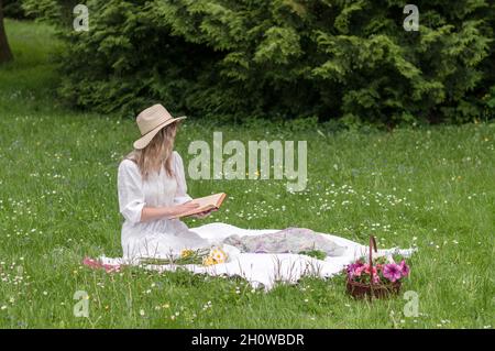 A girl reading a book on a blanket in the forest. Stock Photo