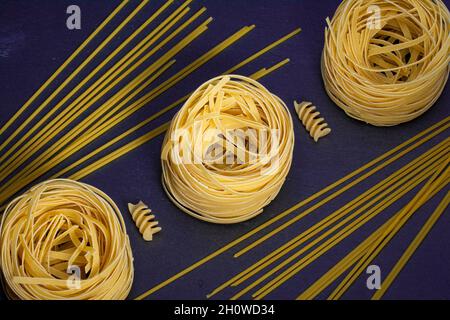 Advertising of different pasta diagonally Mixed pasta, spaghetti, horns, spirals and shells on a blue background for advertising menu. Stock Photo