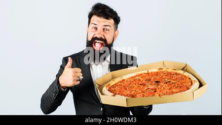 Smiling Businessman with pizza in box shows thumb up. Bearded man in suit with Italian pizza. Fast food. Business lunch. Stock Photo