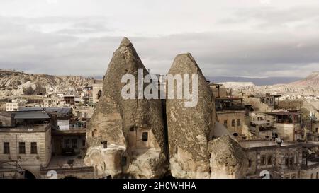 Ancient stone dwellings carved from tuff in Cappadocia, Turkey. Action. Aerial view of unusual beautiful nature, rock formations, city, and cloudy sky Stock Photo