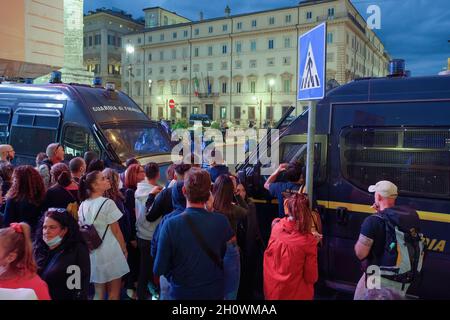 Rome, Italy - October 9 2021: Anti-vax protest against the extension of COVID-19 health pass system. Gathered passing crowd before riot police vehicles, with protesters opposing green pass behind. Stock Photo