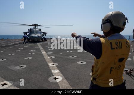 NORTHERN ARABIAN GULF (Oct. 8, 2021) Boatswain’s Mate Seaman Aljevontez Butler uses hand signals to communicate with an MH-60S Seahawk, attached to Helicopter Sea Combat Squadron (HSC) 21, on the flight deck during flight operations aboard the amphibious dock landing ship USS Pearl Harbor (LSD 52), Oct. 8. Pearl Harbor and the 11th Marine Expeditionary Unit are deployed to the U.S. 5th Fleet area of operations in support of naval operations to ensure maritime stability and security in the Central Region, connecting the Mediterranean and the Pacific through the western Indian Ocean and three st Stock Photo