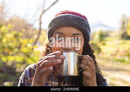 Happy biracial woman drinking coffee and taking break from hiking in countryside Stock Photo