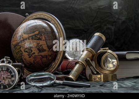 Travel or adventure concept background. Pocket watch, binoculars, antique compass, globe, magnifying glass and stack of books on dark background. Jour Stock Photo