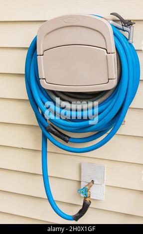 Blue gardening hose hanging on the house wall. Garden hose hangout, wall hose reel. Street photo, selective focus, concept photo equipment for gardeni Stock Photo