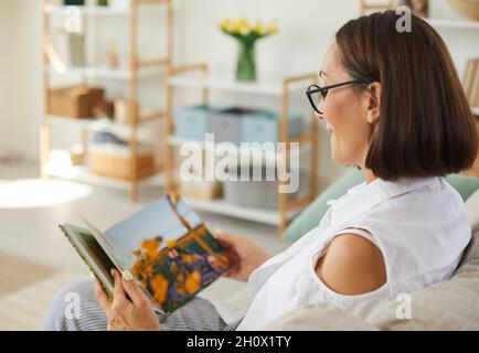 Happy woman sitting on couch and looking through pictures in her family photo album Stock Photo