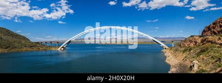 Roosevelt Lake Bridge Panorama. Panoramic of Theordore Roosevelt Lake Bridge in Arizona Sonoran Desert on sunny day with blue sky and fluffy clouds. Stock Photo