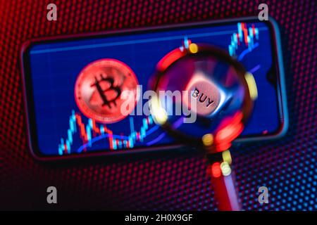 Bitcoin on the background of a smartphone screen with the image of stock candlesticks. Stock Photo