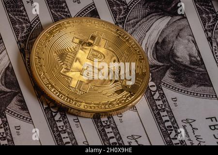 Gold bitcoin on one hundred dollar bills. The coin reflects the eyes of Benjamin Franklin. Stock Photo