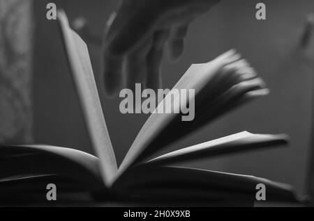 A defocused shot of an old open book and a man's hand. Dusty pages of a hardcover book. Side view. Inside the room. Selective focus. Close-up. Black a Stock Photo