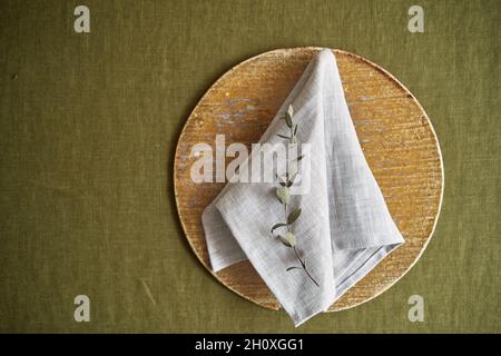Table setting option. A linen grey napkin is neatly folded on a brown plate. Olive background. Stock Photo