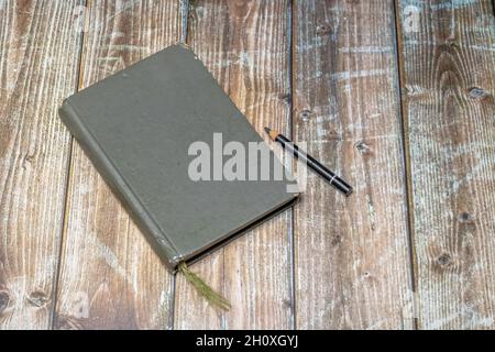 old heavily used closed sketchbook and pencil on a worn brown colored wooden surface Stock Photo
