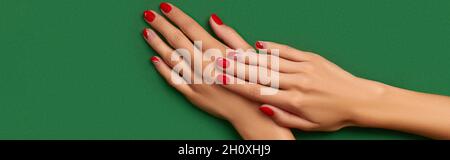Womans hands with trendy christmas red manicure on green background Stock Photo