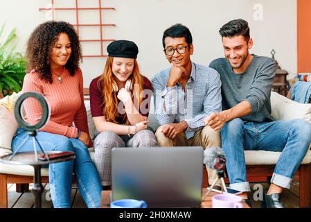 Cheerful multiethnic friends sitting on comfortable sofa and watching movie on laptop in light room in apartment Stock Photo