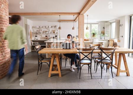 Mother working at home on laptop with son Stock Photo