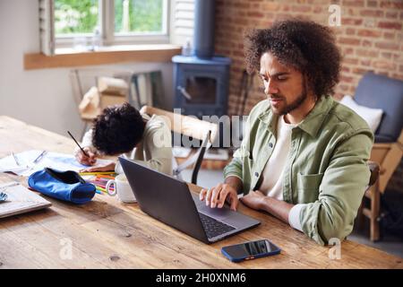 Father using laptop with son drawing at home Stock Photo