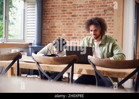 Father using laptop with son doing homework Stock Photo