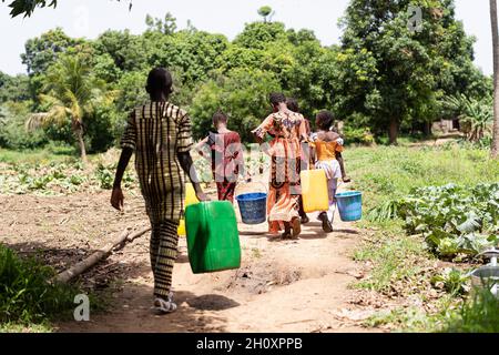 Group of tired black African school-age children busy carrying water back and forth from the village well; child labor concept Stock Photo