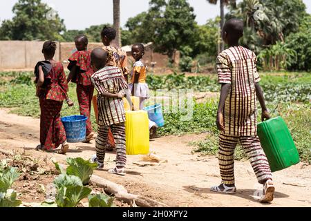Group of black African children carrying empty water containers on their way home from the village well after helping to water the hhelfields Stock Photo