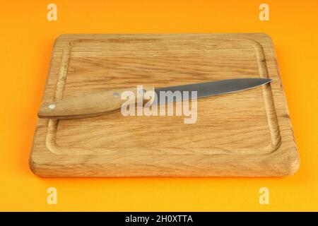 Cutting board with knife on orange background. Stock Photo