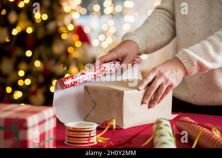 Man and woman preparing for Christmas. Couple in warm sweaters wrapping gifts. Decorated Christmas tree, boxes with presents, colourful wrapping paper Stock Photo