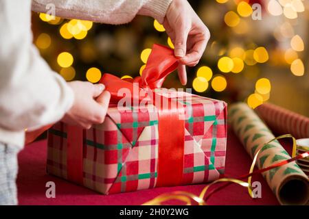 Man and woman preparing for Christmas. Couple in warm sweaters wrapping gifts. Decorated Christmas tree, boxes with presents, colourful wrapping paper Stock Photo