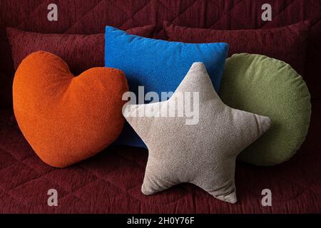 Decor Pillows composition on a couch sofa in modern apartment, home interior. Designed various shapes forms and colors pillows, orange heart, grey sta Stock Photo