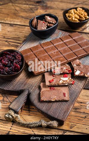 Dark chocolate bar with hazelnuts, peanuts, cranberries and freeze dried raspberries on a wooden board. wooden background. Top view Stock Photo
