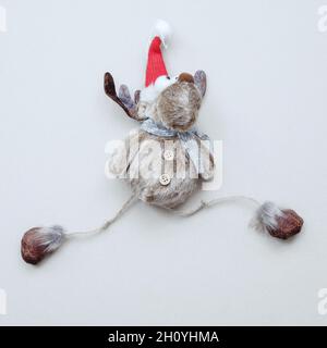 A funny soft toy deer in Santa hat with outstretched legs lies on a white background. Christmas decor. Stock Photo