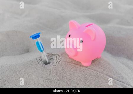 Pink piggy bank and hourglass stands on the white beach sand background. The concept of savings, investments and finances for holidays at sea. Stock Photo