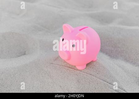 Pink piggy bank stands on the white beach sand background. The concept of savings, investments and finances for holidays at sea.