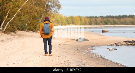 Back view of man in yellow jacket walking along lake - Image Stock Photo