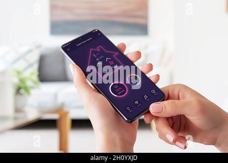 Modern smart home control app on smart phone concept. Woman holding smart phone and controle temperature, light, music and security system Stock Photo