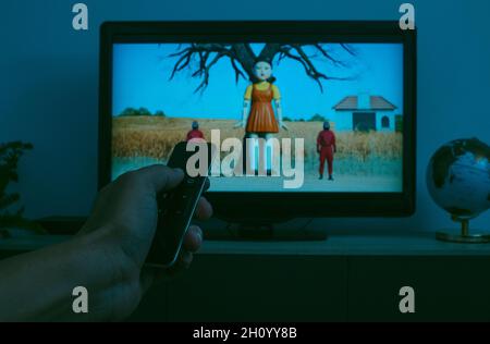 Barcelona, Spain - October 15, 2021: Man watches the TV screening a sequence of the Squid Game, the famous South Korean television series streaming on Stock Photo