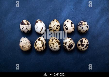 Ten typical patterned quail eggs (with a little gold dust) in two rows on a dark slate serving plate. Stock Photo